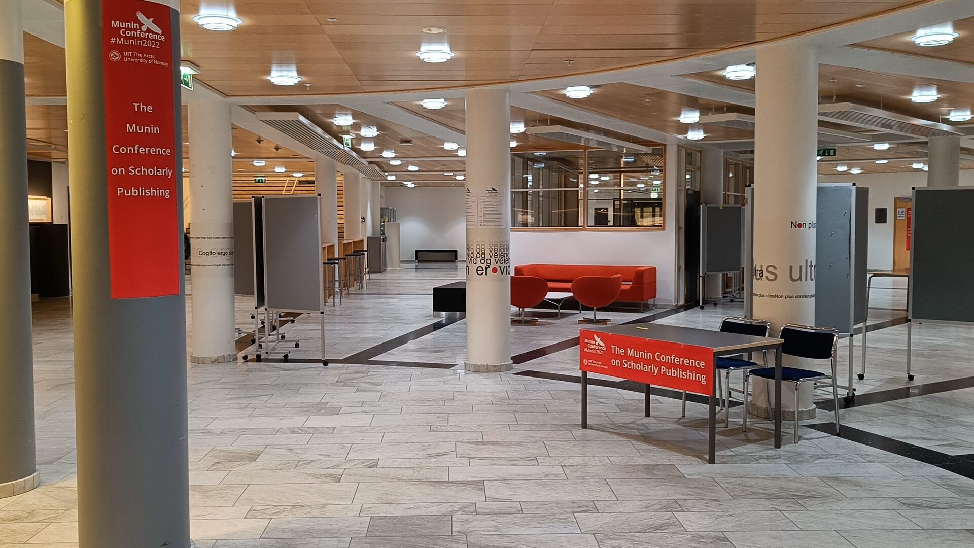Foyer space outside of conference auditoria, with poster stands, chairs and sofas. There are banners with "The Munin Conference on Scholarly Publishing" on some of the furniture.